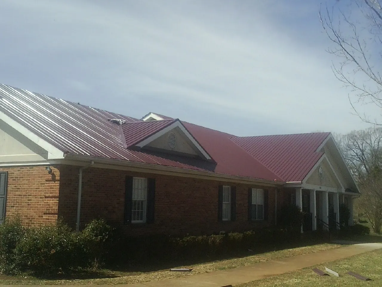 Red metal roof with gabled entries on a long brick building, from a Hail Damage Roof Repair job in Kailua