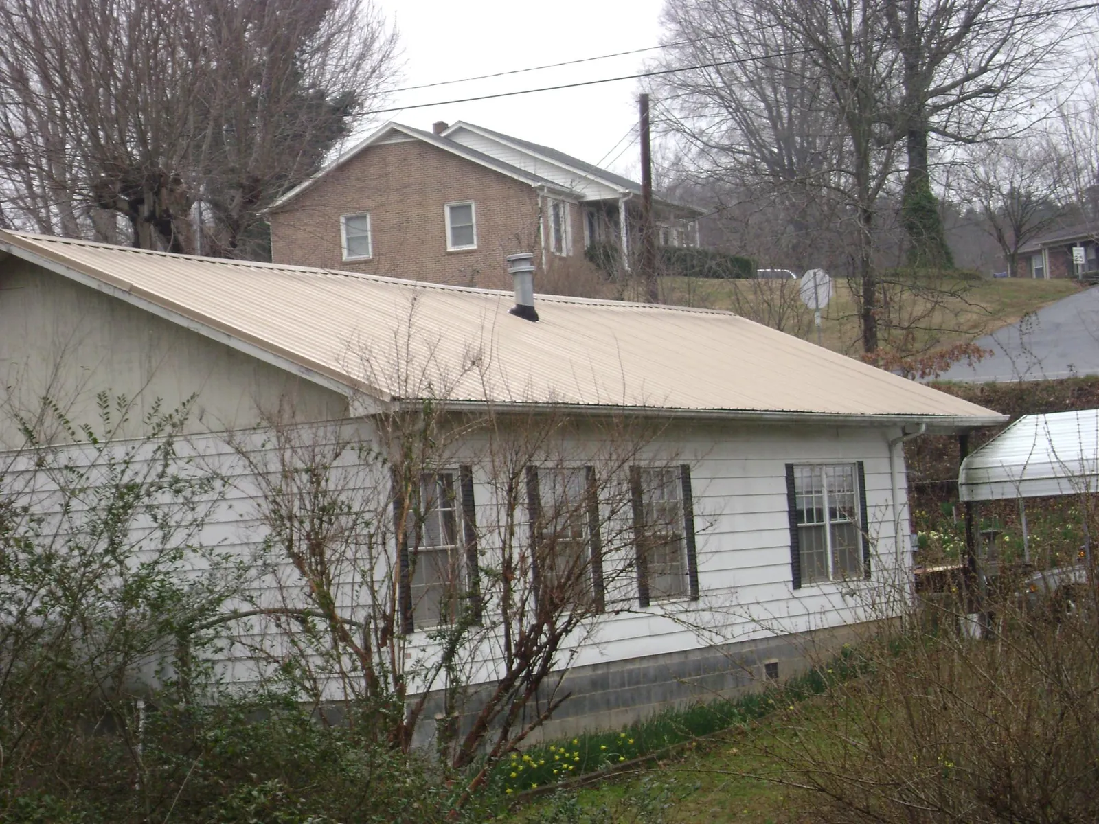 Tan metal roof on a white sided house set into a hillside — Commercial Roofing by Roofing Brothers in Kailua